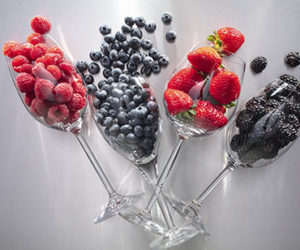 raspberries, blueberries, strawberries, and blackberries falling out of wine glasses