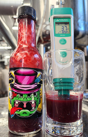 Jar of hot sauce next to a glass partially filled with sauce and a pH meter.