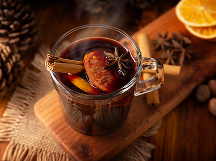 Hot wine or Christmas mulled wine with orange, cinnamon, star anise, clove, nutmeg, and other ingredients on a rustic wooden table.