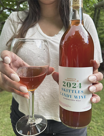 Woman holding a bottle and glass of Skittles Wine.