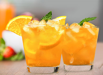 Glasses of an orange wine cocktail with a sprig of mint and ice.
