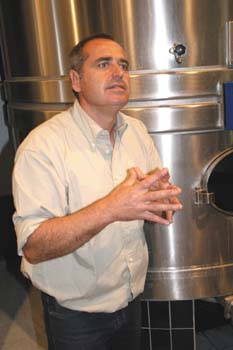 Man stands with hands folded in front of a wine tank.