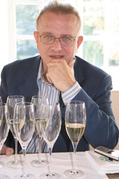 Man wearing glasses and a navy blue sport coat sits at a table with champagne glasses in front of him.