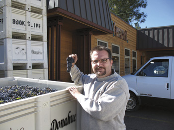 Man wearing glasses standing next to open crate of wine grapes.
