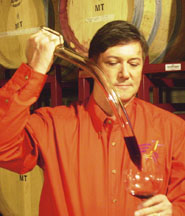 Man uses a wine thief to pour red wine into a glass.