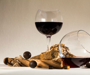 two glasses of red wine with various oak products like chips, balls, and staves.