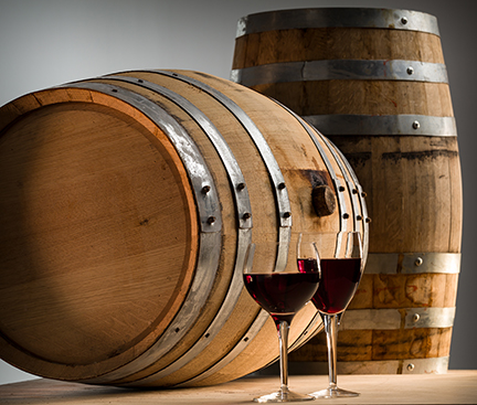 Two glasses with red wine in front of two wine barrels. 