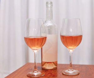 a bottle of rose wine on a table with two full wine glasses