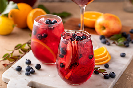 Refreshing summer berry sangria with apples, oranges and blueberry in wine glasses with ice.