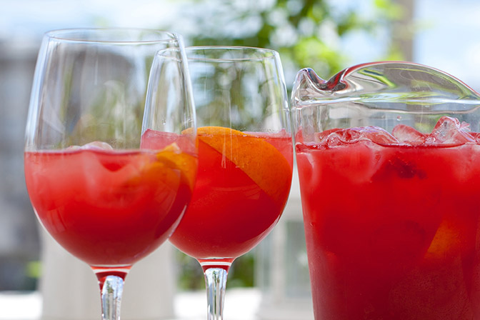 Two glasses of fruit wine with ice next to a pitcher filled with fruit wine and ice.