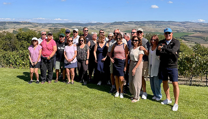 Group of people post for a photo in front of a large Italian countryside and vineyard.