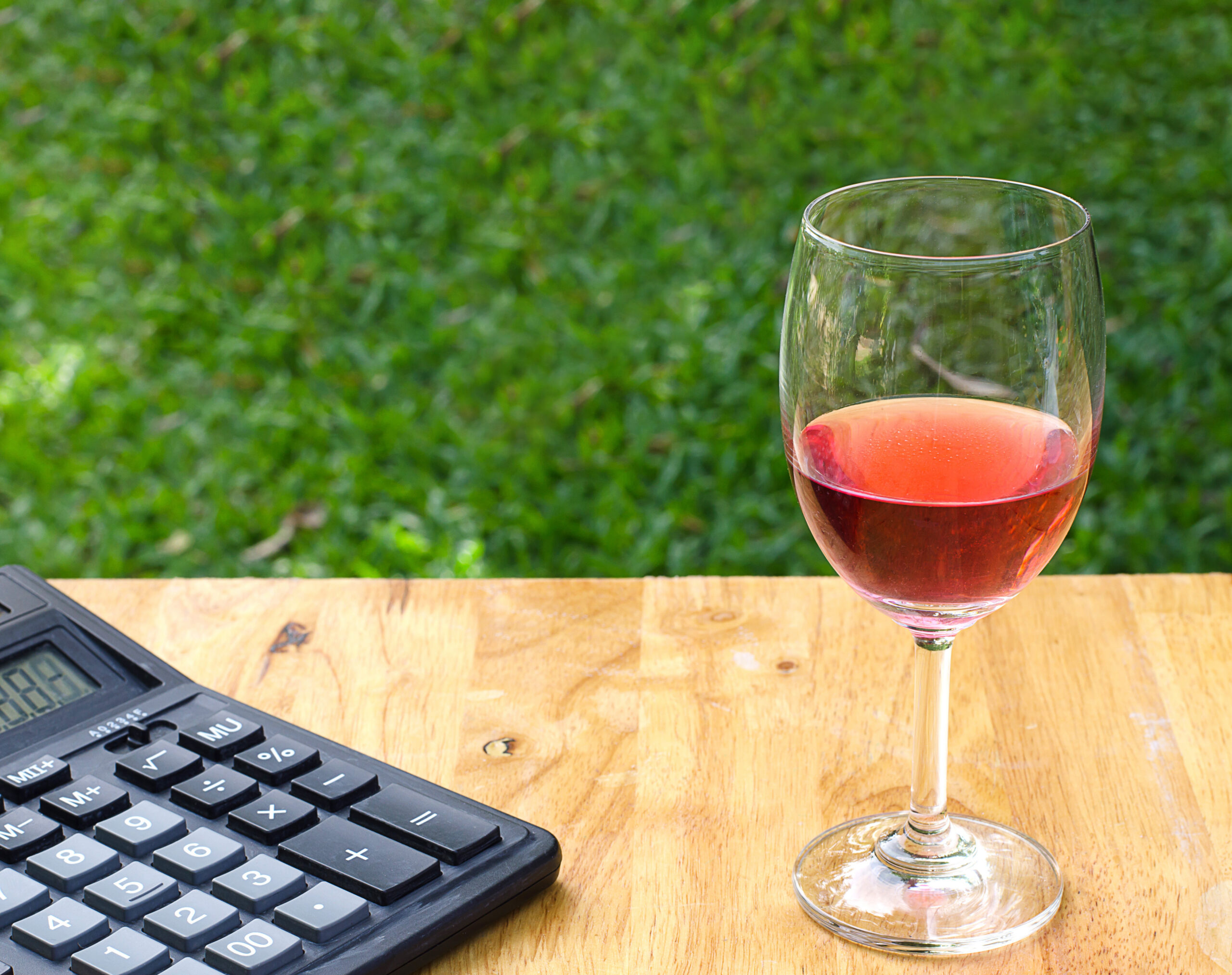 Glass of wine with a calculator on a wooden table.