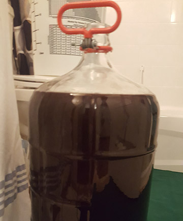 Glass carboy partially filled with red wine.