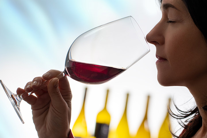 A woman smelling red wine in a glass.